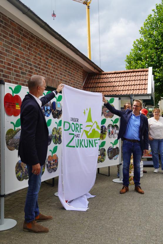 Vorsitzender des Wettbewerbs Ralf Gebken und Ortsbürgermeister Dieter Krieger mit dem Banner „Unser Dorf hat Zukunft“