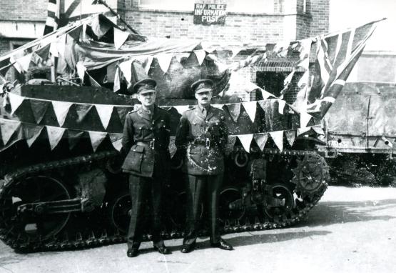 Zwei Offiziere der Militärregierung vor einem mit britischen Flaggen geschmückten Panzer anlässlich der Feier der deutschen Kapitulation.