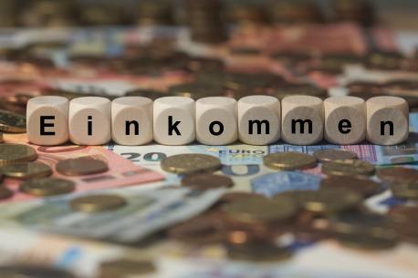 Einkommen - Holzwürfel mit Buchstaben im Hintergrund mit Geld, Geldscheine