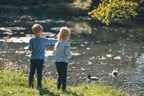 Zwei Kinder die an einem Teich Enten füttern.