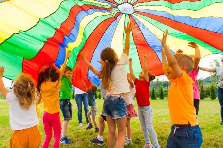 Kinder spielen auf einer Wiese unter einem Schwungtuch.