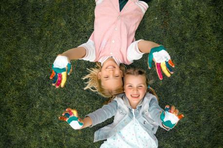 Zwei Mädchen, die auf Rasen liegen, strecken ihre bemalten Hände in die Luft.