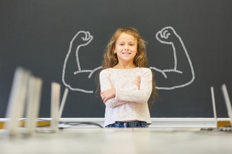 Mädchen in Schule steht vor Tafel mit Muskeln 