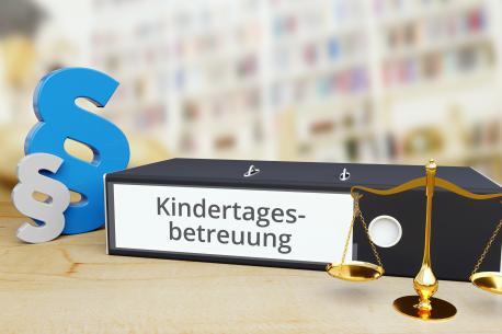 Kindertagesbetreuung-Ordner auf Schreibtisch neben Paragraf und Waage