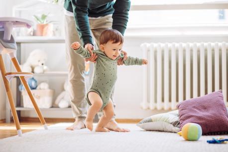 Vater hilft Kleinkind bei den ersten Gehversuchen