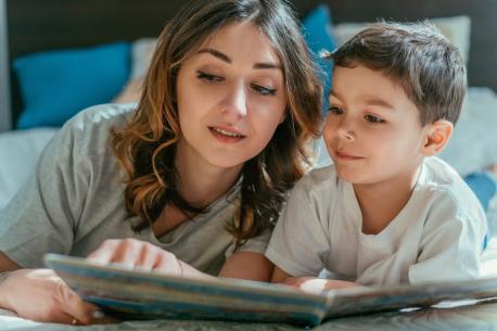 Das Bild zeigt eine Frau und einen Jungen die aufdem Bett liegen, wo die Frau dem Jungen aus dem Buch liest.