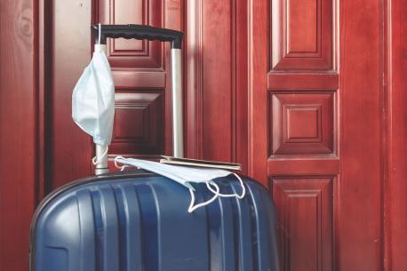 Koffer mit einer Mund-Nase-Maske vor einer Haustür