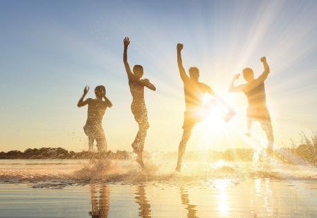 Glückliche junge Menschen laufen und springen am See beim Sonnenuntergang