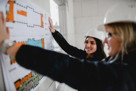 Studenten auf einer Baustelle mit einem Bauplan in der Hand.