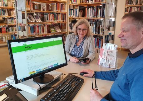 Mitarbeiter vor dem PC, es ist die Homepage der Online-Bibliothek NBib24 geöffnet.